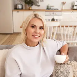 femme blonde assise sur un canapé avec une tasse à la main